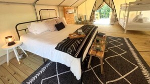 A tented accommodation with a single bed, a small table with a lamp, and a patterned rug. - Luxury Spacious Glamping, Lake View, Grill, Pool, Pet Friendly, Swim (Delta)