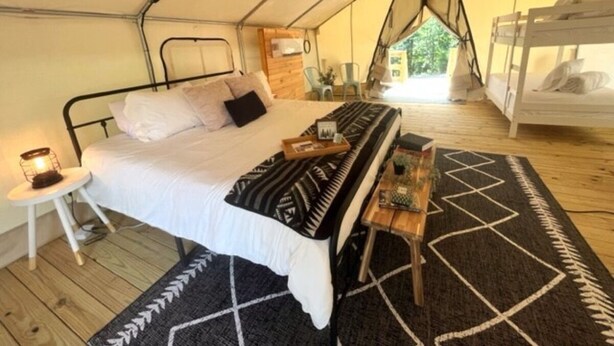 Een tentaccomodatie met een enkel bed, een kleine tafel met lamp en een kamerkleed met patroon.