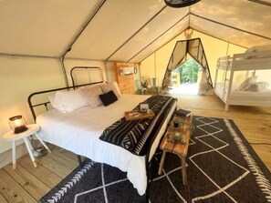 Un hébergement sous tente comprenant un lit simple, une petite table avec une lampe et un tapis à motifs.