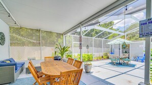 Un'area patio coperta con tavolo e sedie in legno, un divano blu e un cartello con le regole della piscina.