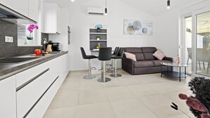 Una cocina moderna con armarios blancos, encimera negra y una zona de comedor con sofá y sillas.