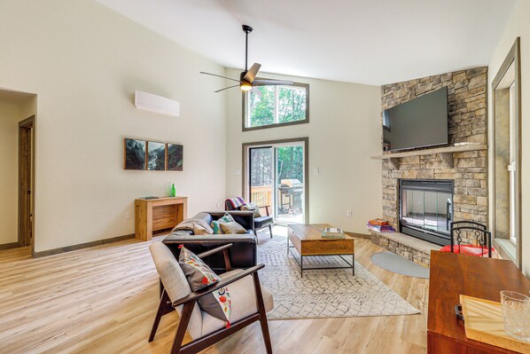 A spacious living room with a fireplace, a ceiling fan, and a large window. - Private Hot Tub: Charming Poconos Cabin! (Albrightsville)