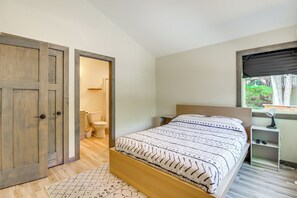 A bedroom with a wooden bed frame, a bedside table, a nightstand, and a window with a view of greenery. - Private Hot Tub: Charming Poconos Cabin! (Albrightsville)