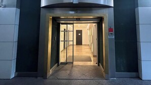 Une entrée dotée d’une porte en verre et d’un cadre métallique, qui donne sur un couloir carrelé, avec une porte au fond.