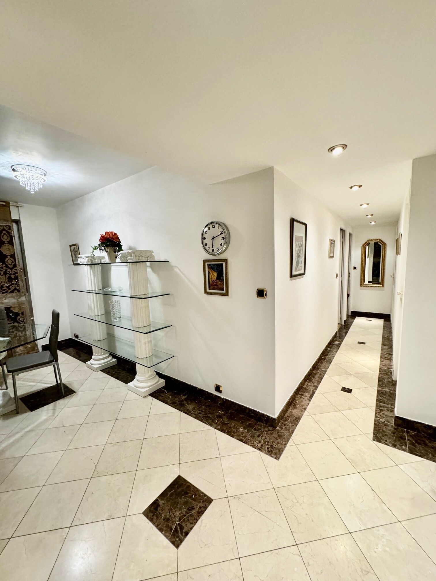 A hallway with a glass display unit, a clock, and a chandelier.