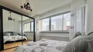Une chambre moderne avec un grand lit, un miroir et une vue sur de hauts immeubles.