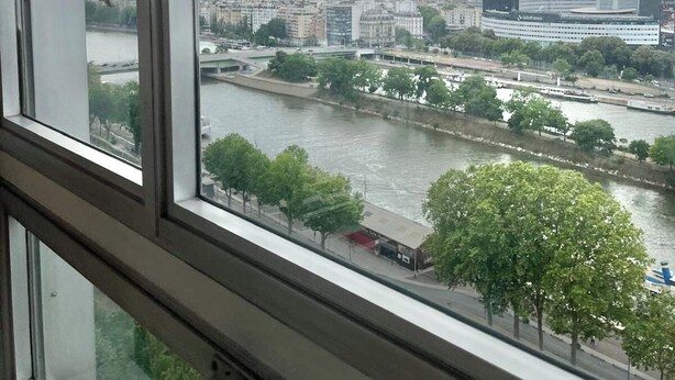 Une vue depuis une fenêtre donnant sur une rivière, avec des bâtiments et des arbres.
