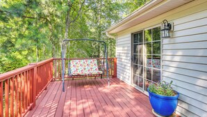 A wooden deck with a swing, a potted plant, and a house with a window and a wall-mounted light fixture. - Lovely McCormick Home in Savannah Lakes Village (McCormick)