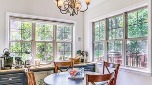 A dining area with a round table, wooden chairs, and a chandelier. Large windows provide views of greenery outside. - Lovely McCormick Home in Savannah Lakes Village (McCormick)