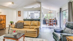 A spacious living room with a leather sofa, a coffee table, and a dining area with a chandelier. - Lovely McCormick Home in Savannah Lakes Village (McCormick)