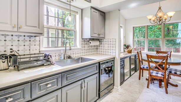 A kitchen with grey cabinets, a large island with a sink, a chandelier, and a dining area with wooden chairs. - Lovely McCormick Home in Savannah Lakes Village (McCormick)