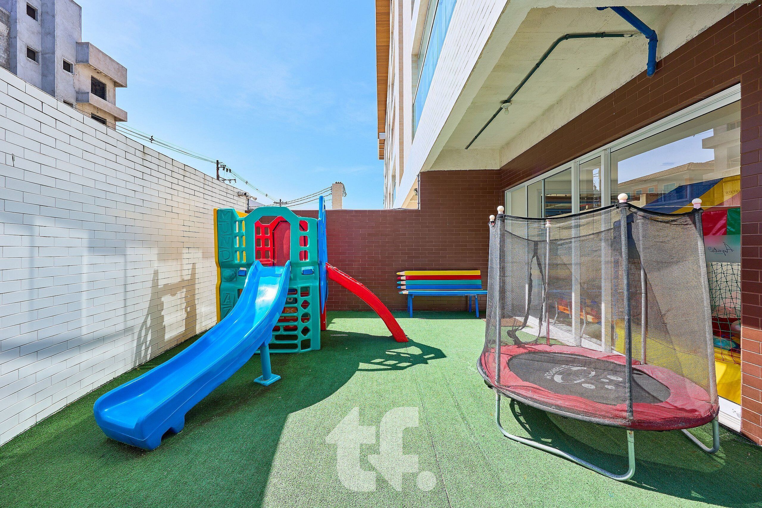Une aire de jeux avec un toboggan bleu, un toboggan rouge et un trampoline.