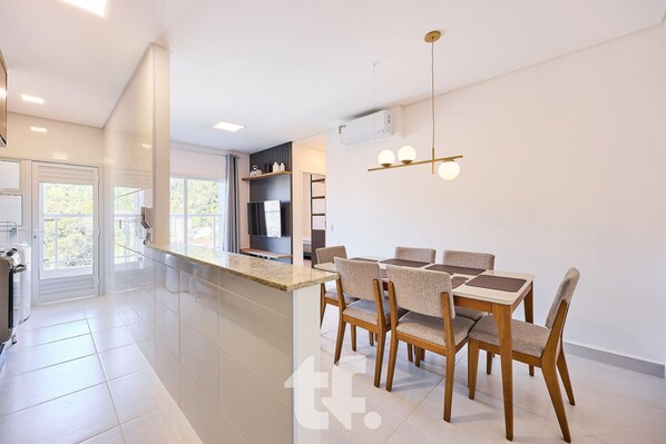 A modern kitchen with a dining area, featuring a kitchen island, a dining table with chairs, and a pendant light. - Residencial Agata (Ubatuba)
