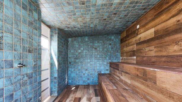 Een badkamer met blauwe mozaïektegels, houten vloeren en een houten bankje.