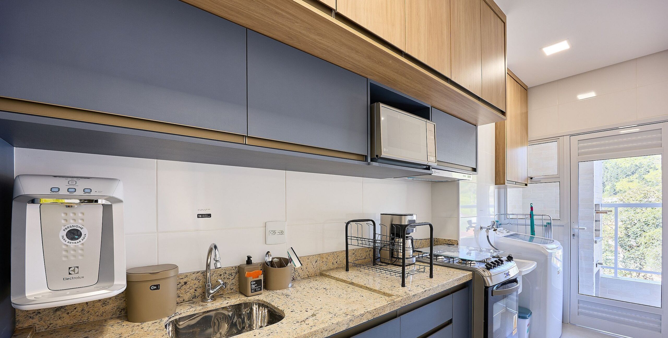 A modern kitchen with a built-in water dispenser, stainless steel appliances, and a large window offering a view of greenery.