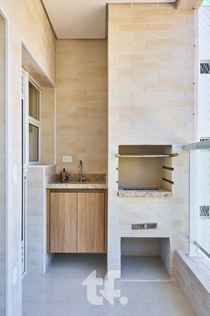 A modern kitchen with a built-in oven, wooden cabinets, and a window above the sink. - Residencial Agata  (Ubatuba)