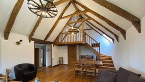 A spacious loft with high ceilings, exposed wooden beams, a dining area with a wooden table and chairs, a large window, and a staircase leading to an upper level. - New gîte in vimenet (Aveyron) medieval village between aubrac and lévézou  (Vimenet)
