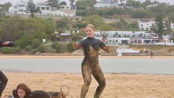 A beach scene with people in wetsuits, some standing on surfboards, and others lying on the sand.
