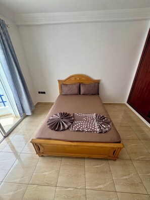 A single bed with a wooden headboard, two pillows, and decorative pillows on a tiled floor.
