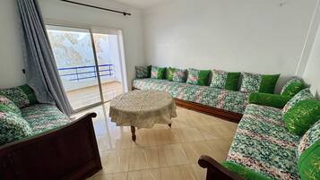 A living room with a sofa set, a round table, and a view through a sliding door.