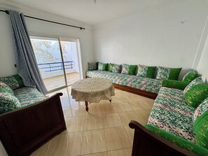A living room with a sofa set, a round table, and a view through a sliding door.