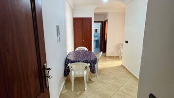 A hallway with a wooden door, a dining area with a table and chairs, and a ceiling light fixture.