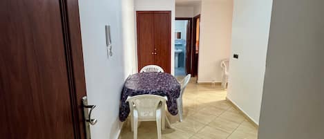 A hallway with a wooden door, a dining area with a table and chairs, and a ceiling light fixture.