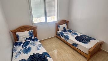 A bedroom with two wooden beds, a ceiling fan, and a window with blinds.