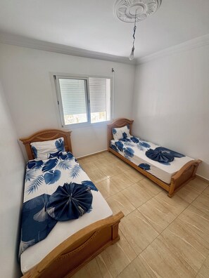 Une chambre avec deux lits en bois, un ventilateur de plafond et une fenêtre avec des stores.