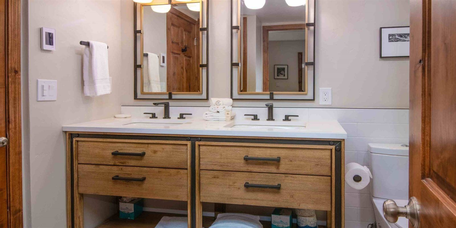 A bathroom with a double sink, wooden vanity, two drawers, a mirror, and a toilet.