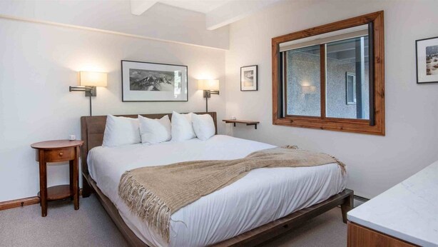 Una camera da letto con un letto grande, due comodini, lampade a parete, quadri incorniciati e una finestra con vetro satinato.