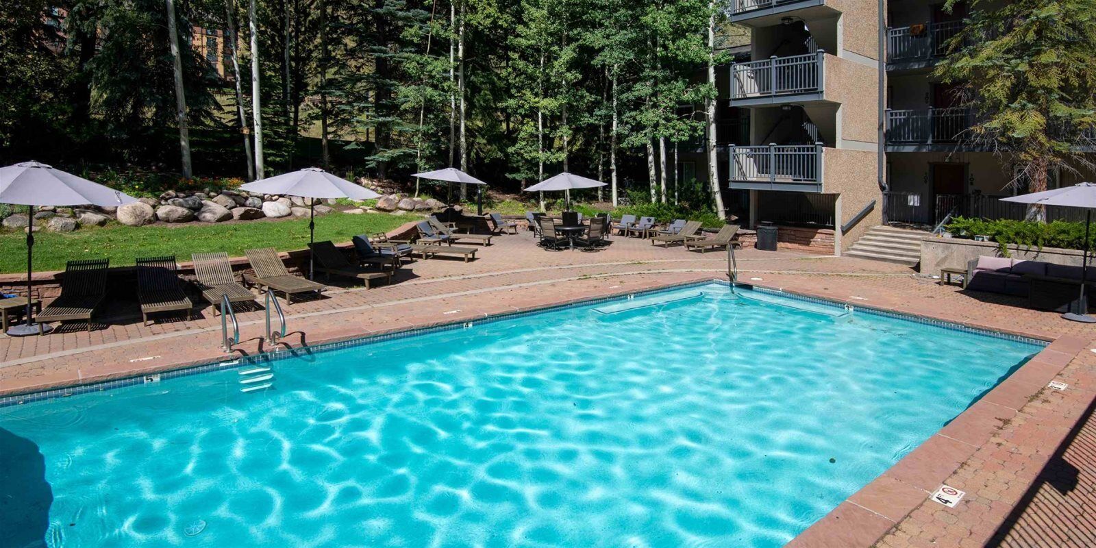 Une piscine rectangulaire à l’eau d’un bleu cristallin, entourée de chaises longues et de parasols.