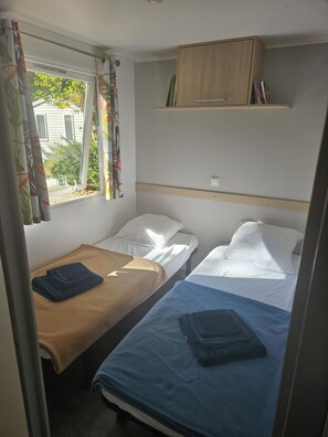 A compact room with two single beds, a wooden cabinet above, and a window with curtains.