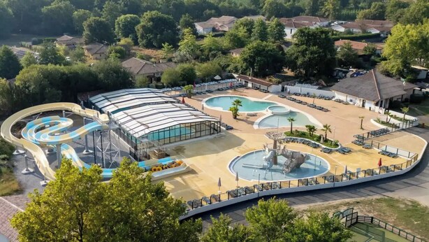 Luftaufnahme eines Resorts mit Wasserpark, darunter ein Wellenbecken, ein Lazy River und ein überdachter Bereich mit Liegestühlen.
