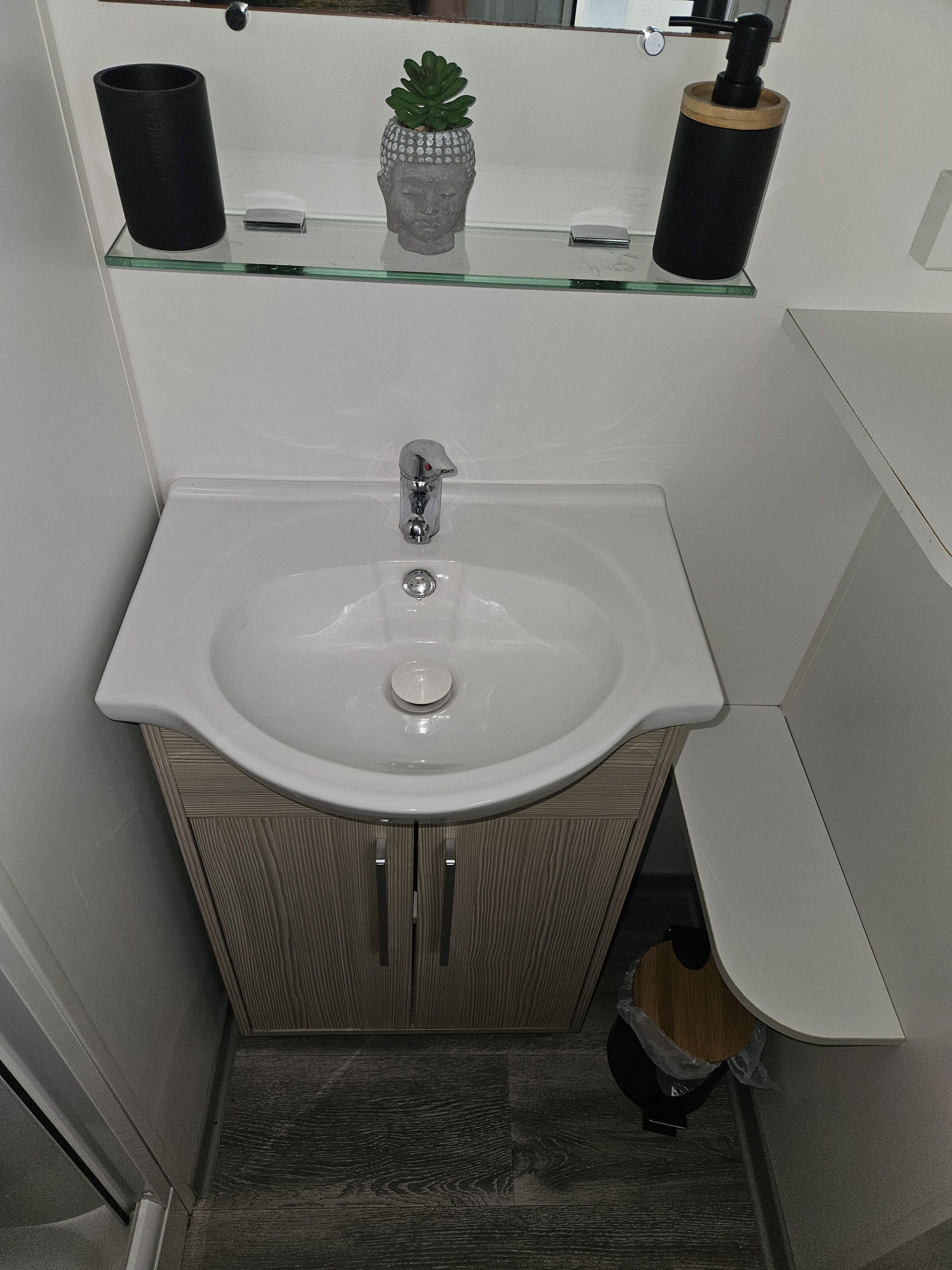Ein Badezimmer mit einem weißen Waschbecken, einem Holfach und einer kleinen Topfpflanze auf dem Regal.