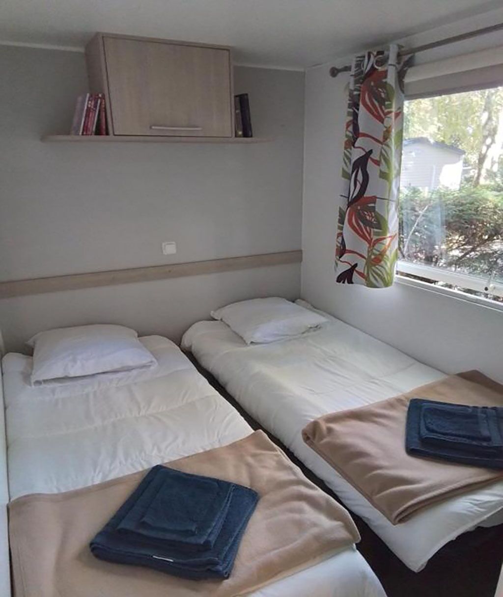 Une chambre avec deux lits simples, un meuble en bois placé au-dessus et une fenêtre avec un rideau.