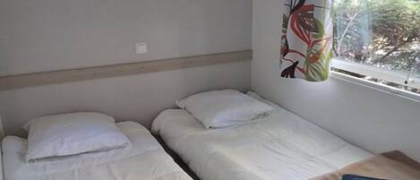 Une chambre avec deux lits simples, un meuble en bois placé au-dessus et une fenêtre avec un rideau.