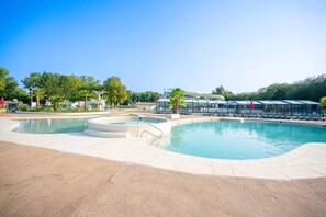 A large outdoor swimming pool with a circular hot tub, surrounded by lounge chairs and covered seating areas.