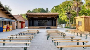 Ein Amphitheater im Freien mit Bühne und Sitzbereich, umgeben von Bäumen und Gebäuden.