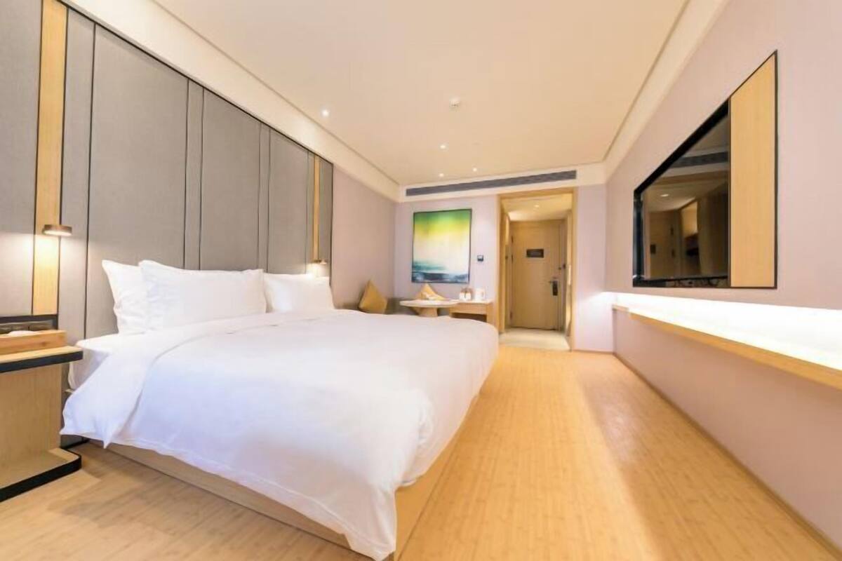 A modern hotel room with a large bed, wooden flooring, a flat-screen TV, and a minimalist design.