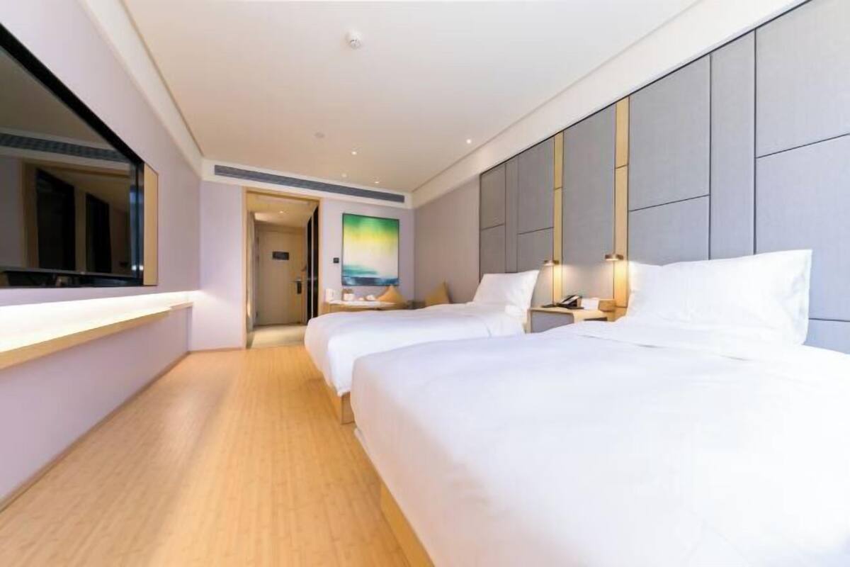 A hotel room with two beds, a large mirror, a painting on the wall, and a wooden floor.