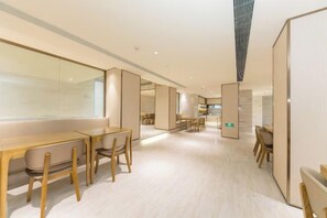 A modern interior with long tables and chairs, a kitchen area, and a large window.