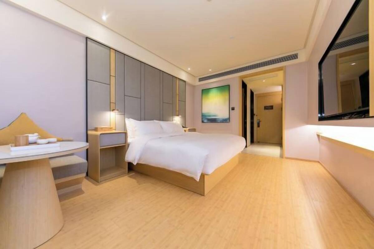 A modern hotel room with a bed, bedside table, and a painting on the wall.