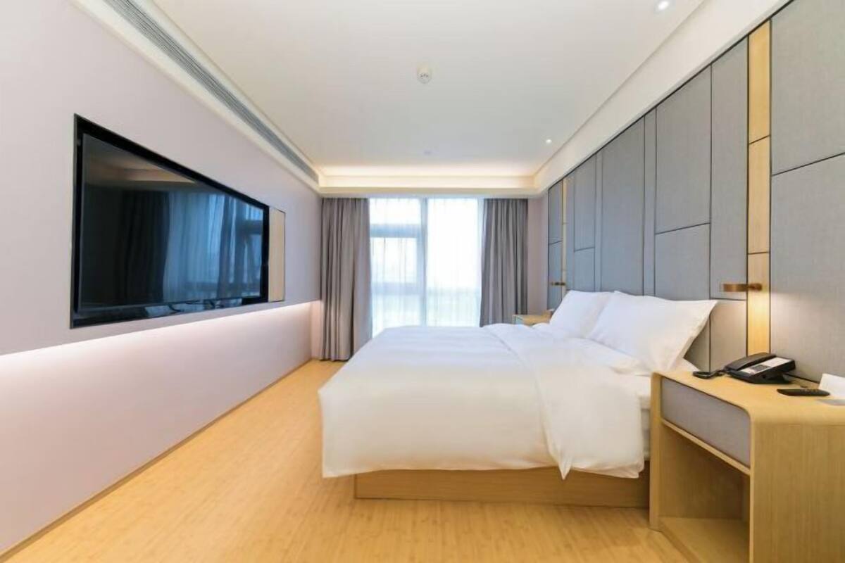 A modern hotel room with a large bed, a bedside table with a phone, and a window with curtains.