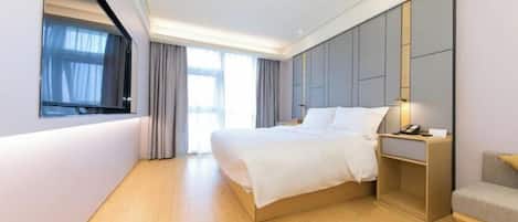 A modern hotel room with a large bed, a bedside table with a lamp, and a view of the outdoors through a window.