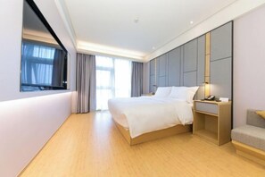 A modern hotel room with a large bed, a bedside table with a lamp, and a view of the outdoors through a window.