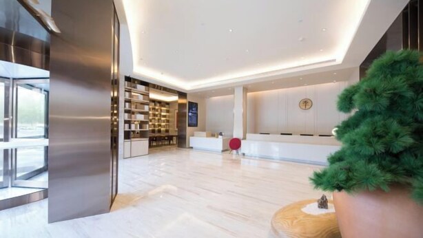 A modern hotel lobby with a reception desk, a large bookshelf, and a potted tree. - JI Hotel (Jiaxing Zhongshan Road) (Jiaxing)