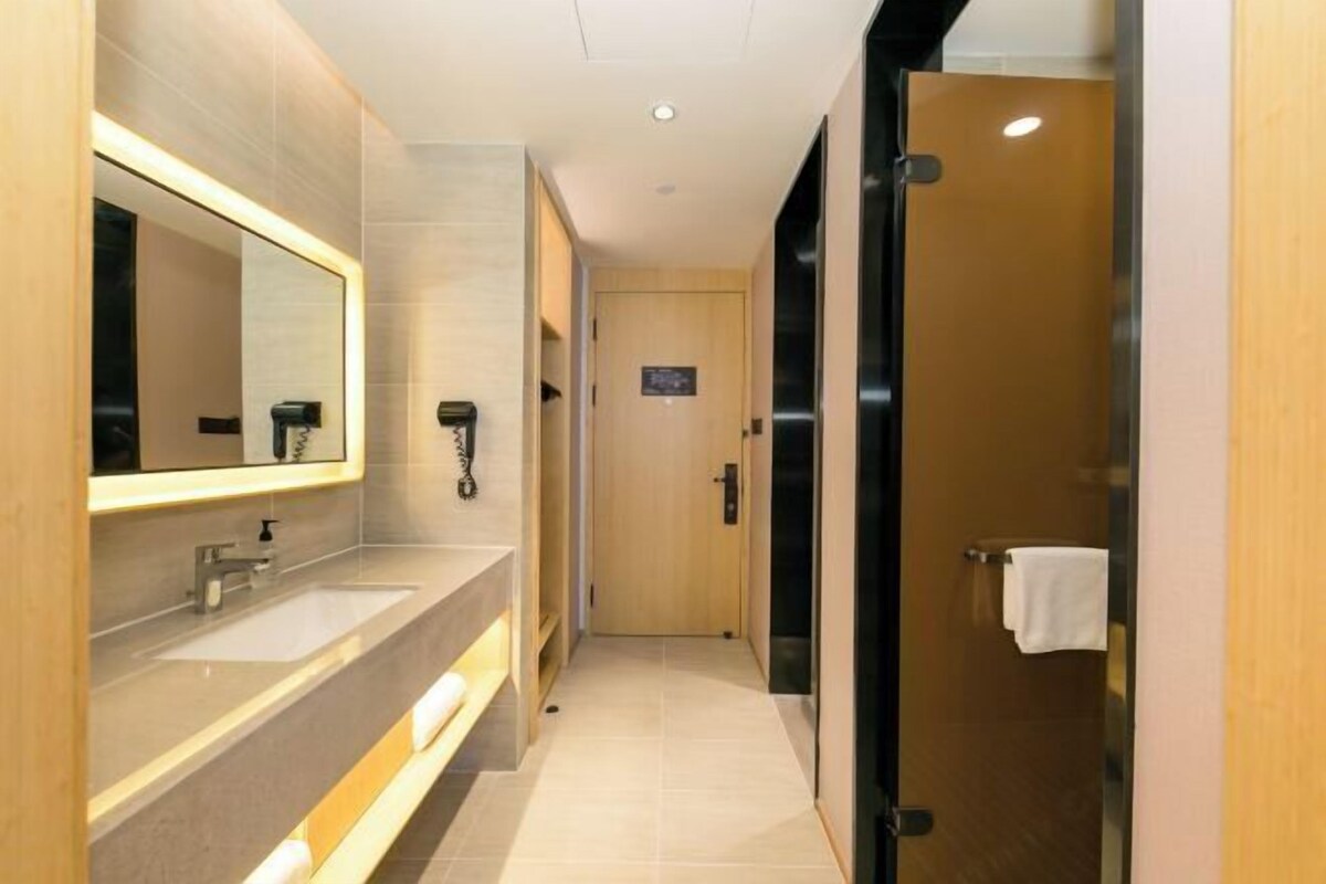 A modern bathroom with a large mirror, two sinks, a towel rack, and a door leading to another room.