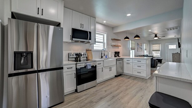 A modern kitchen with stainless steel appliances, white cabinetry, and a central island. - Nautical Nest - 1 block to the Beach, Newly Renovated (Galveston)