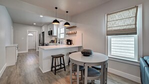 A modern kitchen with a central island, pendant lighting, and a dining area with a round table and stools. - Nautical Nest - 1 block to the Beach, Newly Renovated (Galveston)